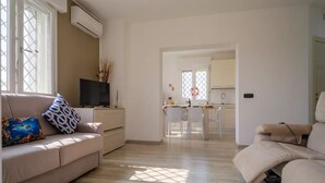 A spacious living room with a beige sofa, a television, and a dining area with a kitchen in the background.