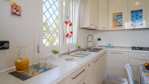 A modern kitchen with white cabinets, a stainless steel sink, and a window with a life preserver decoration.