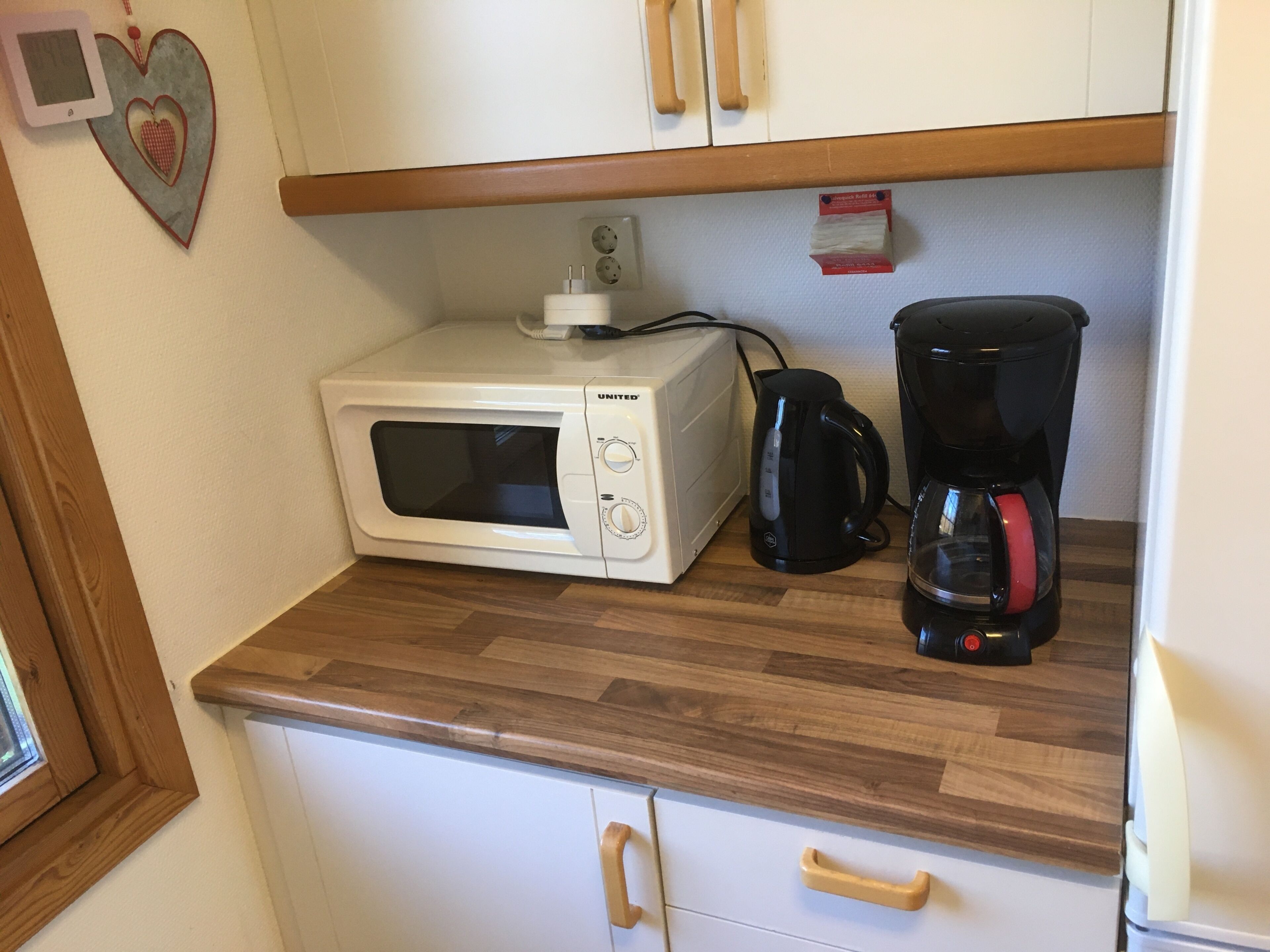 Een keuken met een magnetron, een zwarte koffiezetapparaat en houten kastjes.