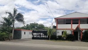 Un hotel llamado "HOTEL PISCALONGA" con un estilo arquitectónico moderno, que presenta una entrada destacada y un camino de acceso con portón.