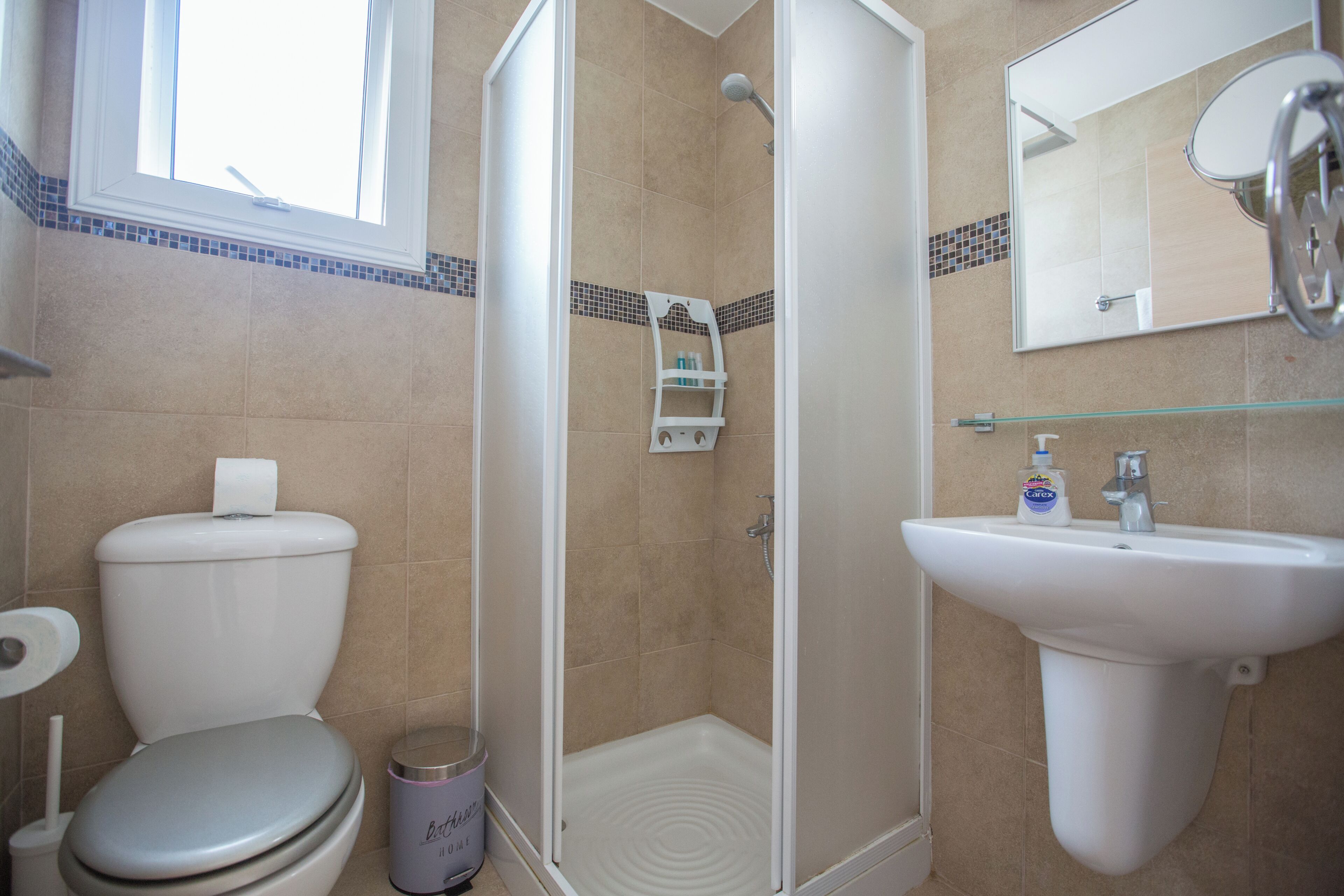 A bathroom with a toilet, shower, sink, and a mirror.