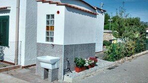 A building with a white exterior, a tiled lower section, a small white sink, and a potted plant with red flowers.