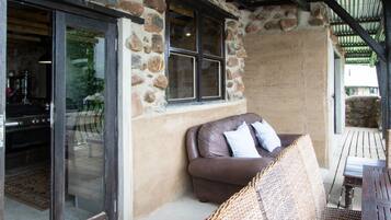 Pared exterior de piedra con un ventanal grande, una silla de mimbre y una mesa de madera.
