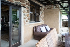 A stone exterior wall with a large window, a wicker chair, and a wooden table. - Boutique Lake Villa Description (Greater Kokstad)