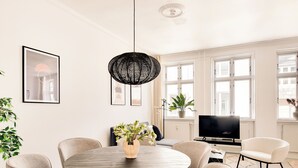 A modern living room with a round dining table, comfortable chairs, a black woven light fixture, a flat-screen TV, and large windows with white frames. - City 2- Cosy 1 Bdr Apt In the Center of Copenhagen (Copenhagen)