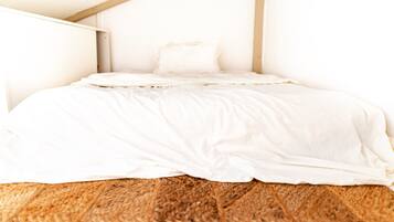 Une chambre avec un plancher en bois, un lit blanc et un plafond en pente.