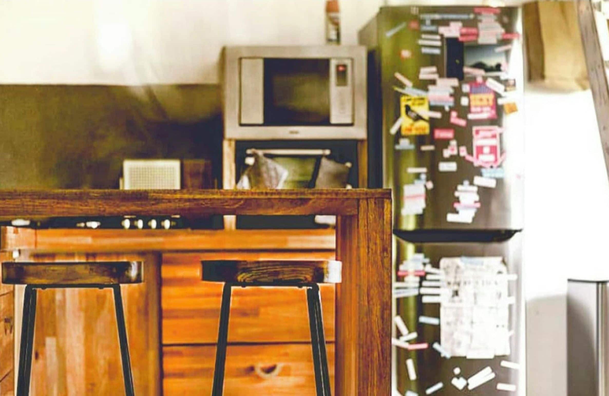 A kitchen with wooden stools, a microwave, and a refrigerator with notes attached.