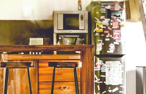 A kitchen with wooden stools, a microwave, and a refrigerator with notes attached.
