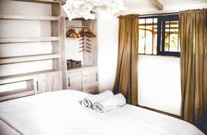 A neatly made bed with rolled towels, a wardrobe with hanging clothes, and a window with curtains. - Ti Bout Paradi Ti Zil (Tamarin)