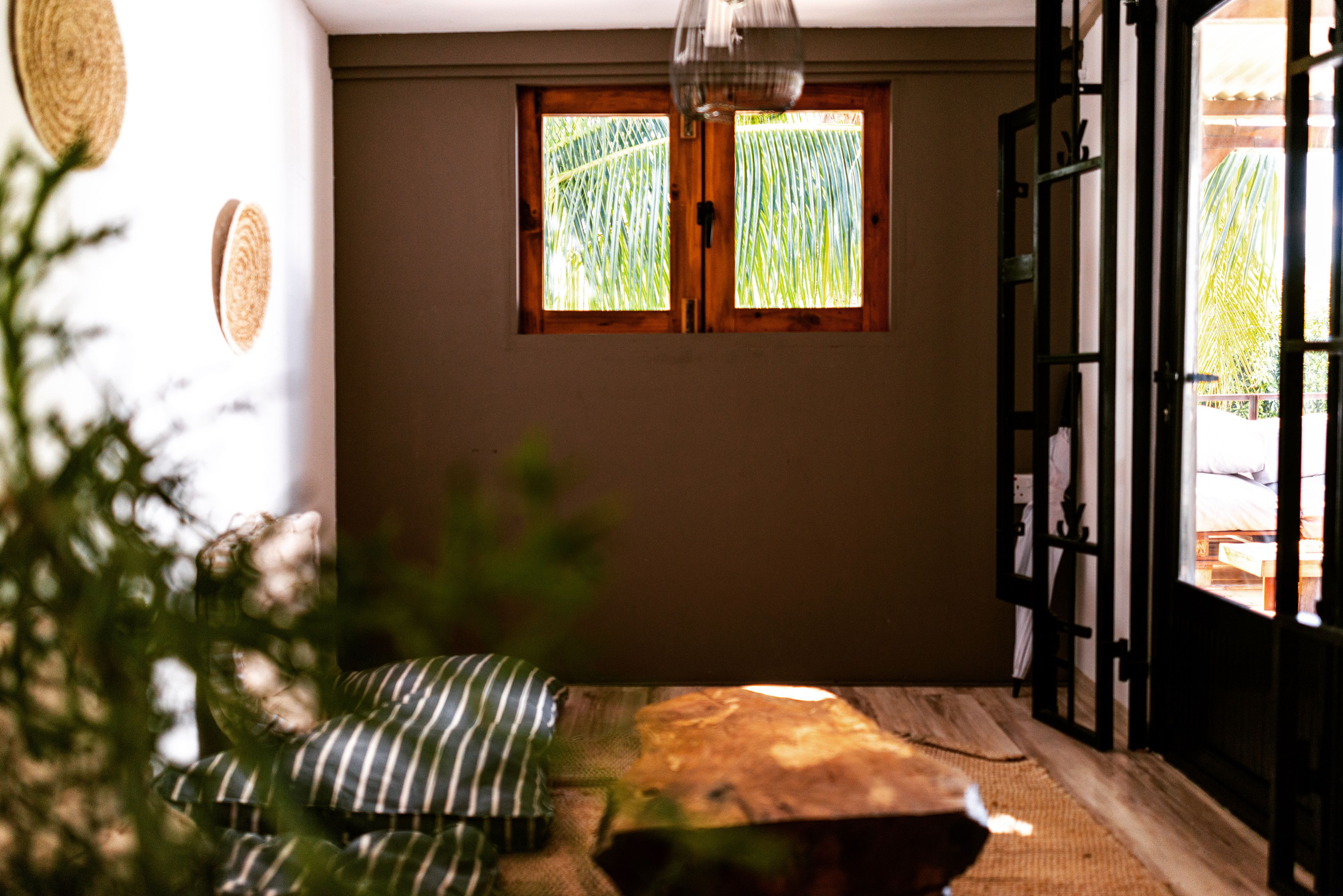 A room with a bed, a window with a view of greenery, and a door leading outside.