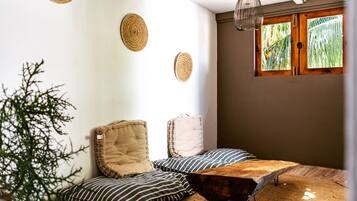 Un coin salon accueillant avec une table en bois, des coussins à rayures et des éléments décoratifs tissés accrochés au mur.