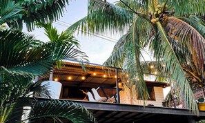 A tropical setting with a building featuring a corrugated metal roof and a balcony with hanging lights. - Ti Bout Paradi Ti Zil (Tamarin)