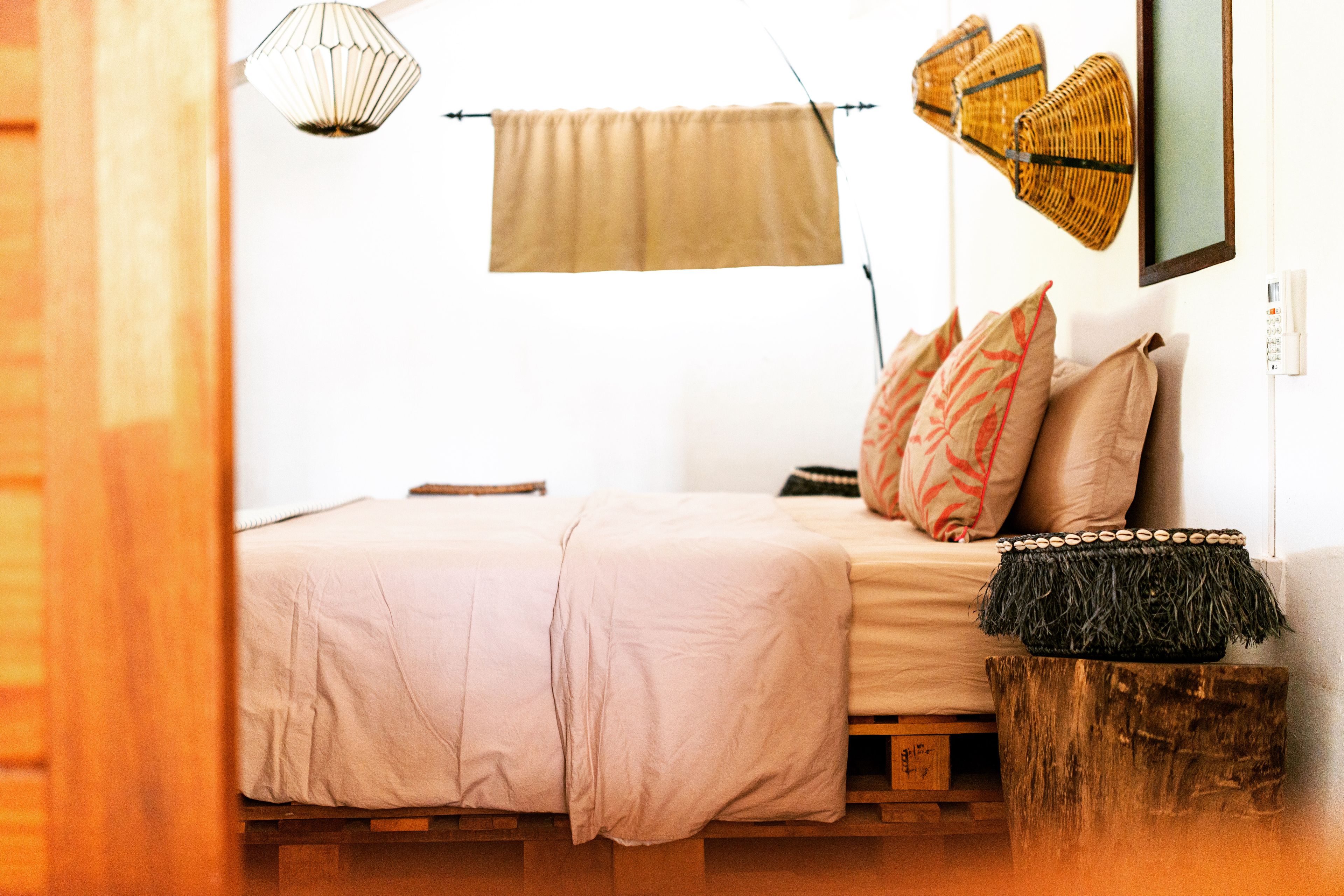 A bed with a beige bedspread, a wooden headboard, and a woven basket on a wooden stool.