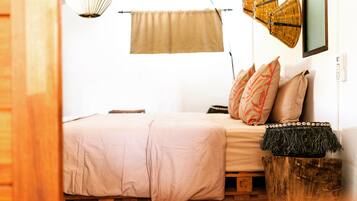 A bed with a beige bedspread, a wooden headboard, and a woven basket on a wooden stool.