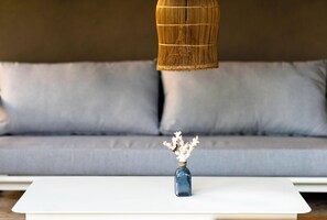 A white table with a blue vase containing dried flowers, positioned in front of a grey sofa. - Ti Bout Paradi Ti Zil (Tamarin)