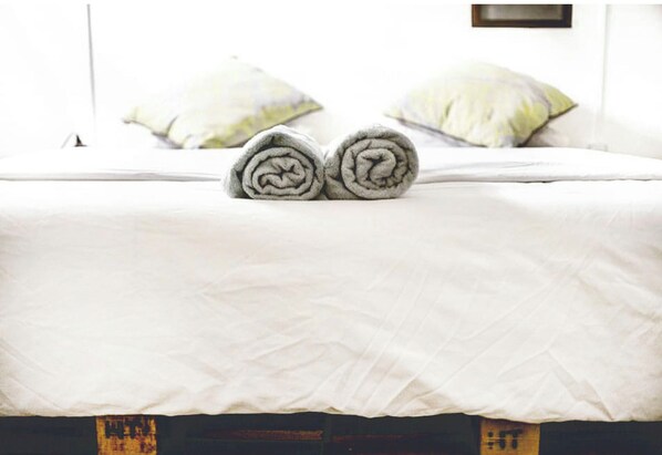 A neatly made bed with rolled towels in the center, a white bedspread, and two pillows on the bed.