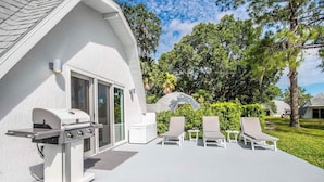 Een modern terras buiten met een barbecue, lounge stoelen en uitzicht op weelderige begroeiing.