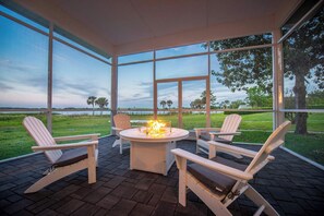 A covered outdoor seating area with a fire feature and chairs facing a scenic view.