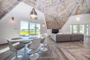 A spacious room with a high ceiling, a dining area with modern chairs and a table, a sofa, and a television.