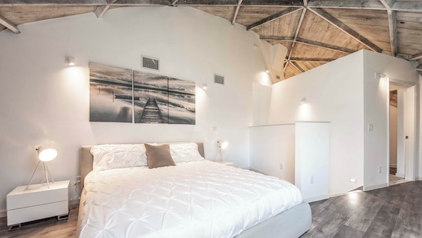 Een slaapkamer met een groot bed, twee bedlampen, een nachtkastje en een kunstwerk aan de muur.