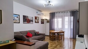 Un soggiorno con divano, tavolo da pranzo con sedie, televisore e lampadario.