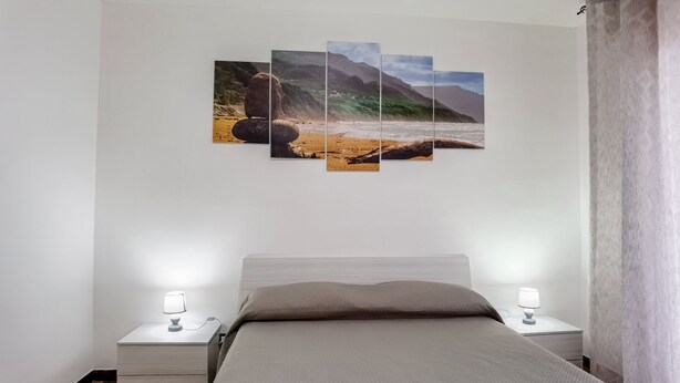 Una camera da letto con un letto, due comodini con lampade e un'opera d'arte a più pannelli appesa al muro che raffigura una spiaggia.