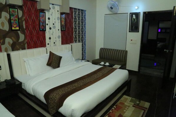 A hotel room with a large bed, a bedside table, a chair, and a door leading to a bathroom. - The Mirage Palace Hotel (Kisumu)