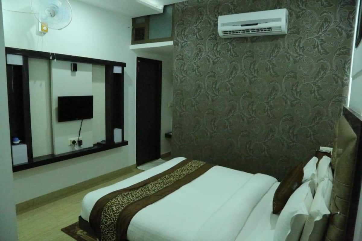 A hotel room with a bed, a television, an air conditioner, and a patterned wall.