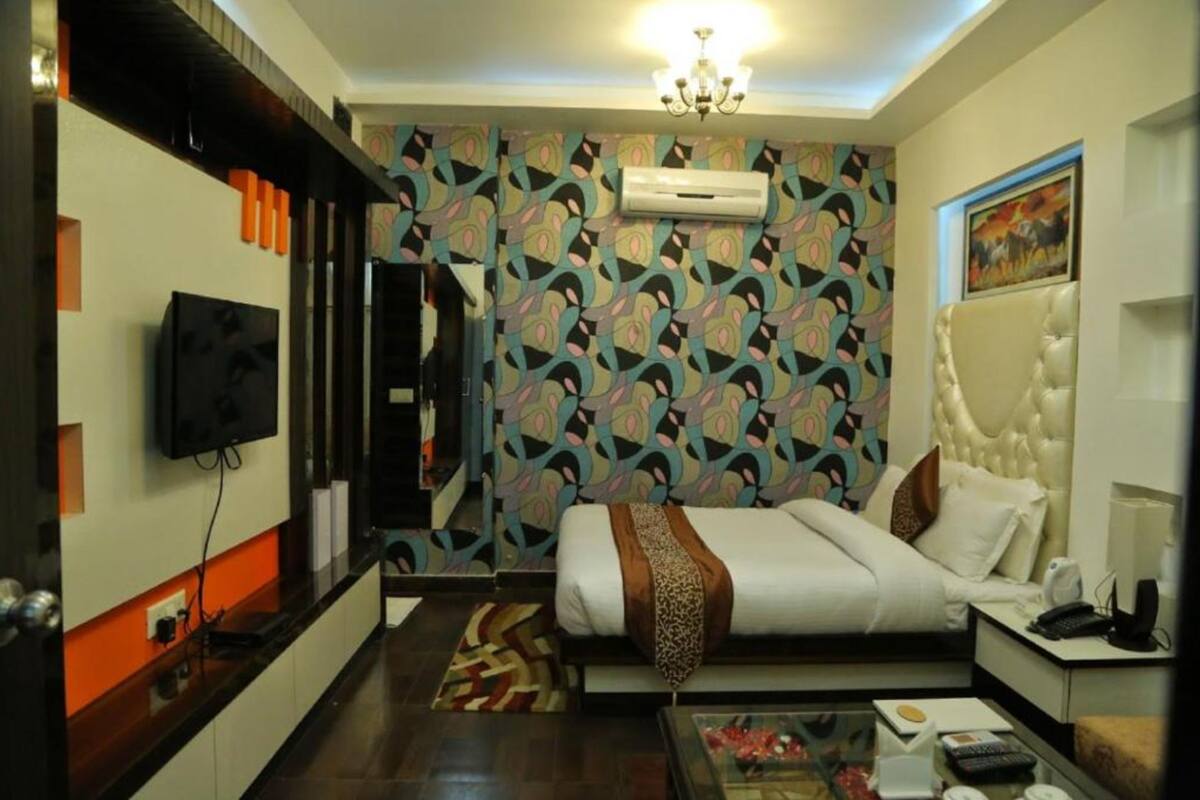 A hotel room with a bed, a TV, a desk, and a patterned wall.