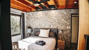 Ein Schlafzimmer mit Steinwand, Bett mit weißer Bettdecke, Holzboden und Nachttisch mit Lampe.