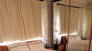 Uma cama grande com colcha acolchoada, duas mesas de cabeceira com luminárias, e uma cama de dossel ao fundo.