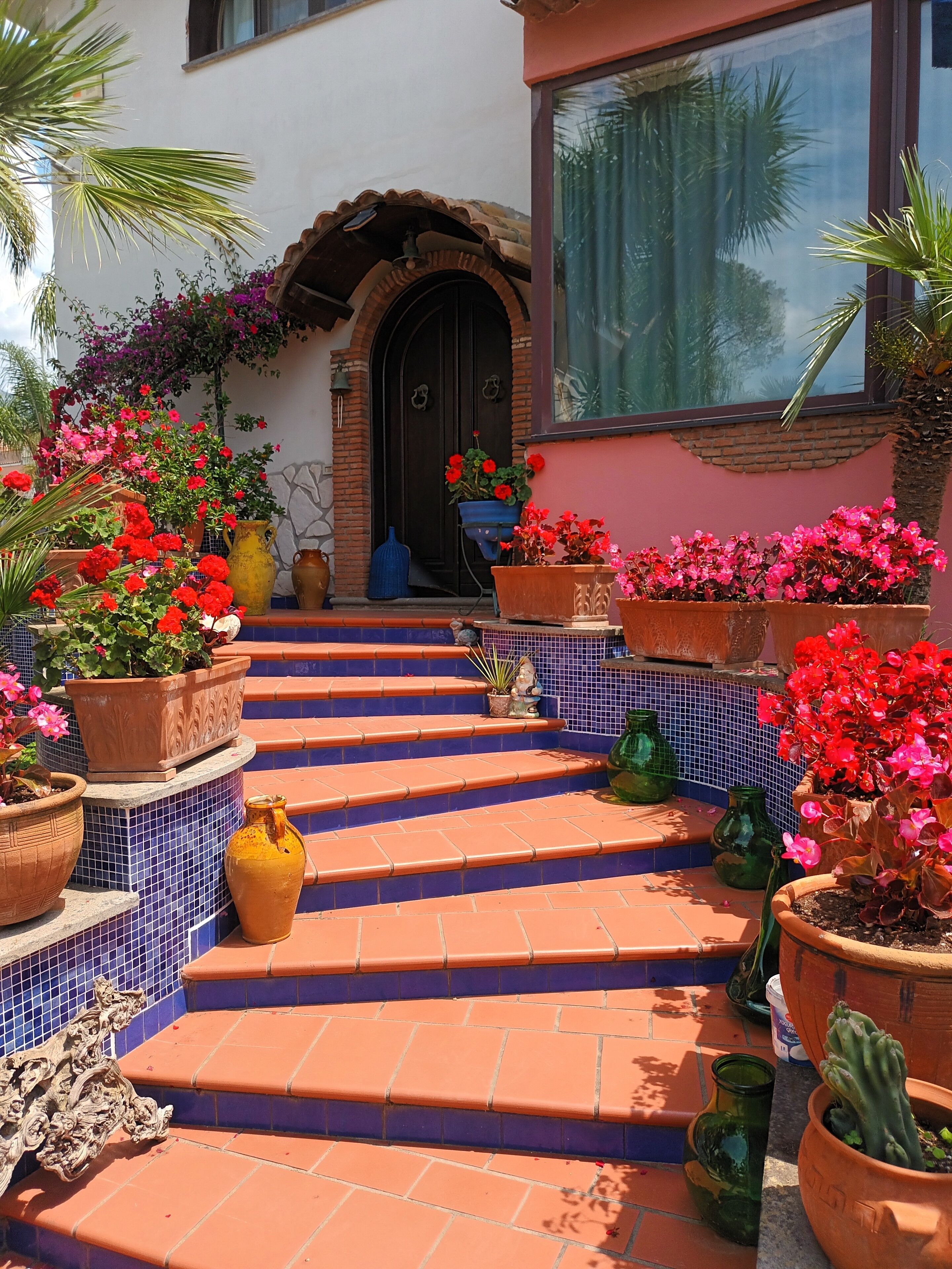 A set of terracotta steps leading to a door with a decorative archway, surrounded by potted plants and flowers.