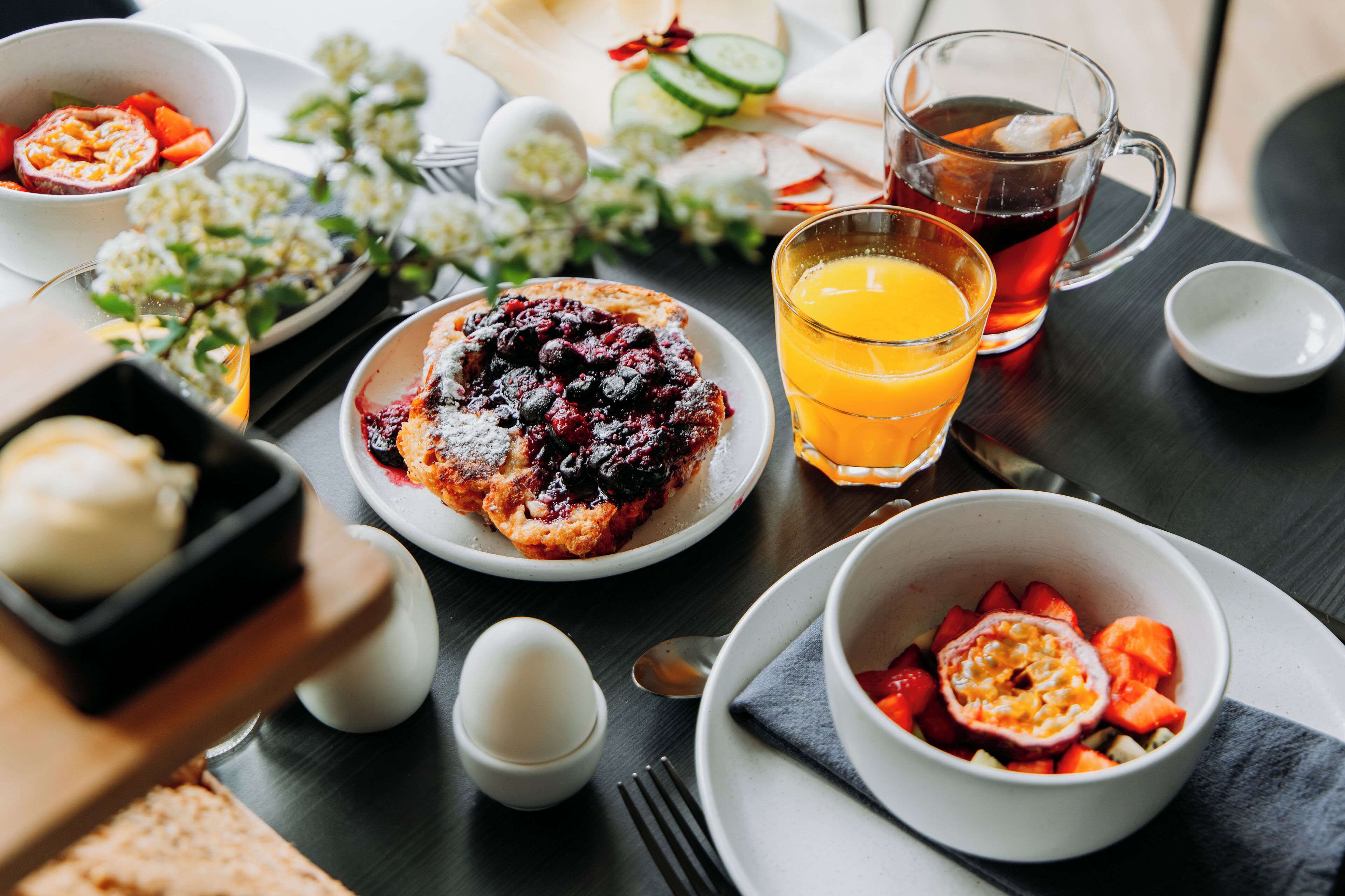A breakfast setting with a variety of dishes including a berry compote, a glass of orange juice, and a cup of tea.