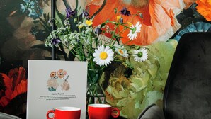 Una mesa con un jarrón de flores, un certificado enmarcado y dos tazas rojas.