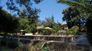 Un muro de piedra con un jardín, una piscina y un edificio con tejado de baldosas.