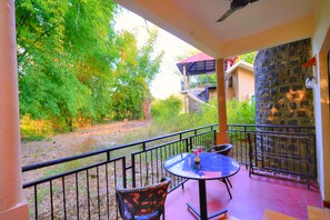 Ein Balkon mit Tisch und Stühlen, der auf einen Garten mit Bäumen und einem Gebäude im Hintergrund blickt.