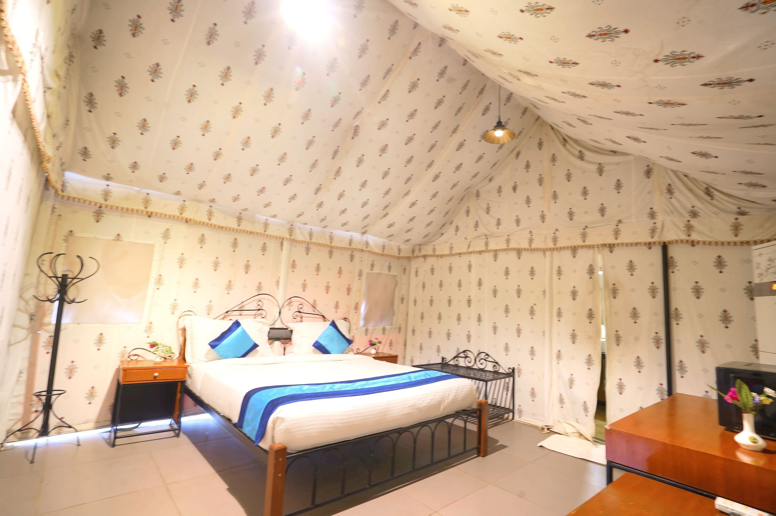 A bedroom with a bed, a nightstand, a desk, and a lamp.