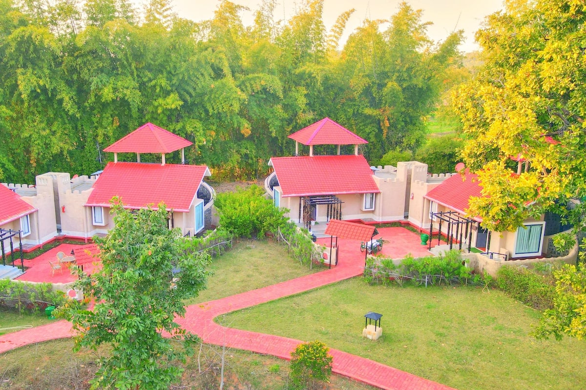 A castle-themed hotel with multiple red-roofed buildings, a central courtyard, and surrounding lush greenery.