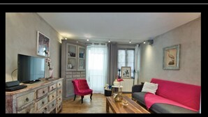 A living room with a television, a red chair, a grey sofa, and a wooden coffee table.