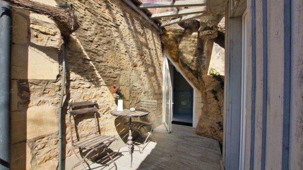 A narrow stone corridor with a wooden table and chairs, a door, and a small window.