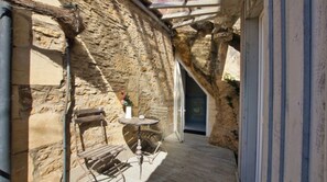 A narrow stone corridor with a wooden table and chairs, a door, and a small window.