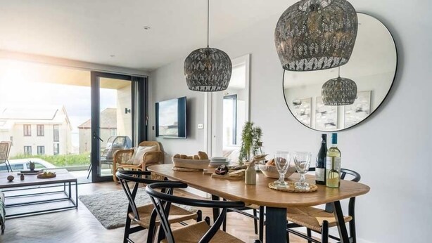 Un comedor moderno con una mesa de madera, sillas negras y dos lámparas colgantes.