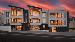 Un moderno edificio residencial de varios pisos con amplios ventanales y balcones, que presenta un diseño arquitectónico contemporáneo.