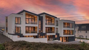 Una casa moderna de varios pisos con amplios ventanales y balcones, sobre un cielo al atardecer.