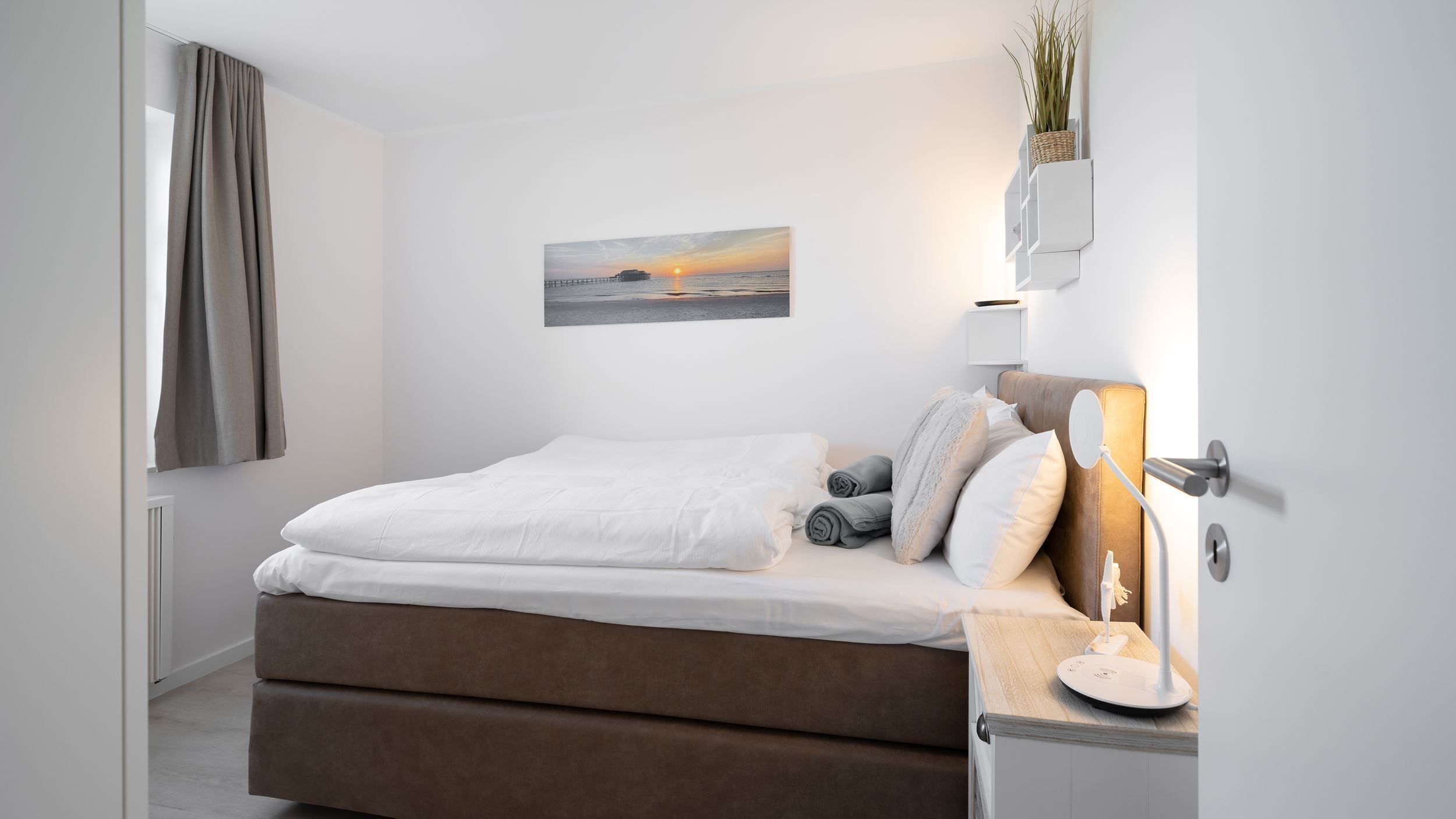 Ein modernes Schlafzimmer mit einem Bett, Nachttisch, Lampe und einem Bild an der Wand.
