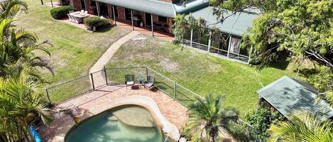 A house with a swimming pool, surrounded by lush greenery and a well-maintained lawn.