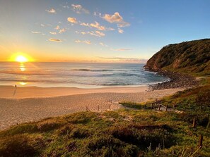 A beach with a wooden walkway leading to the water, surrounded by greenery.