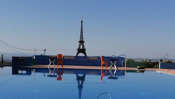 A pool with a view of the Eiffel Tower, surrounded by orange chairs and a sign that says "Femme".