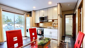 A modern kitchen with white cabinets, a microwave, and a stove. There is a glass dining table with red chairs and a small plant on the table. - Cabin Compound | Lake + Alpine Lookout | Fast Wifi (Twin Lakes)