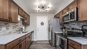 A modern kitchen with wooden cabinets, a stainless steel refrigerator, a microwave, a stove, and a dishwasher.